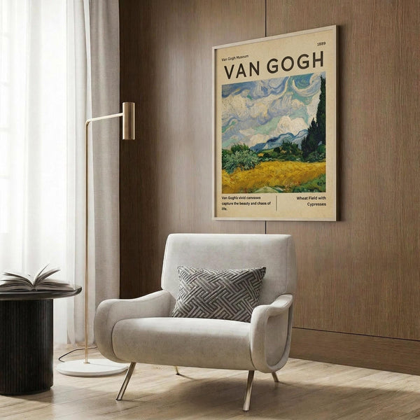 May include: Van Gogh museum poster featuring Wheat Field with Cypresses painting displayed on wood-paneled wall above beige upholstered chair with geometric patterned pillow. Modern brass floor lamp and dark round side table with open book visible. Poster shows swirling blue sky over golden wheat field with dark cypress trees, cream-colored background with black text.