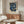 May include: Framed botanical poster with blue floral pattern featuring ornate flowers and foliage in William Morris style, displayed above wooden sideboard in modern living room with cream upholstered chair, glass coffee table, and minimalist decor