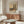 May include: Vintage-style poster featuring Wassily Kandinsky's landscape artwork with two prominent poplar trees, displayed in a modern living room setting above a wooden sideboard. The poster shows earthy tones of green, orange, and yellow in an expressionist style, framed and mounted on a light gray wall. Scene includes a white curved chair, glass coffee table, floor lamp, and table lamp creating a mid-century modern aesthetic.