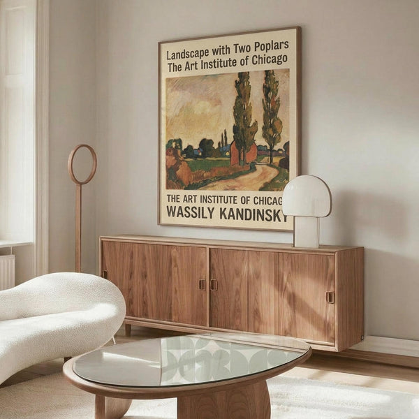 May include: Vintage-style poster featuring Wassily Kandinsky's landscape artwork with two prominent poplar trees, displayed in a modern living room setting above a wooden sideboard. The poster shows earthy tones of green, orange, and yellow in an expressionist style, framed and mounted on a light gray wall. Scene includes a white curved chair, glass coffee table, floor lamp, and table lamp creating a mid-century modern aesthetic.