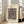 May include: Framed abstract art print leaning against white wall next to beige upholstered chair in bright living room. Poster features geometric shapes, lines, and symbols in muted brown and beige tones within cream-colored mat and light wood frame. Natural sunlight streams through tall windows creating soft shadows on hardwood floors.