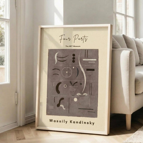 May include: Framed abstract art print leaning against white wall next to beige upholstered chair in bright living room. Poster features geometric shapes, lines, and symbols in muted brown and beige tones within cream-colored mat and light wood frame. Natural sunlight streams through tall windows creating soft shadows on hardwood floors.