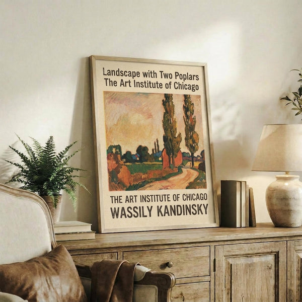 May include: Framed art print featuring a colorful landscape painting with two tall poplar trees, winding path, and buildings in warm oranges and greens, displayed on a rustic wooden sideboard alongside potted plants, books, and ceramic vases in a cozy living room setting with neutral tones and natural lighting.