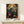 May include: Framed botanical art print featuring a blue bird perched among ornate flowering branches with red peonies and cream blooms in William Morris decorative style. Print displays in thin wooden frame on light wood console table beside small wrapped white gift box with evergreen sprig. Cream colored wall background with soft natural lighting.