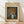 May include: Framed Van Gogh poster print leaning against white wall on wooden floor. Shows vibrant orange poppies in white vase against blue background. Cream-colored poster with brown text header and artwork details. Natural wood frame with thin profile. Soft natural lighting creates diagonal shadows across white textured wall.