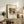 May include: Framed art print of Wassily Kandinsky's abstract painting featuring flowing organic forms in earth tones of brown, orange, yellow and green, displayed on a rustic wooden console table alongside decorative pottery, books, and a fern plant in a neutral-toned living room setting.