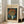 May include: Framed poster print of Van Gogh's orange poppies in white vase painting displayed on light wooden floor beside beige upholstered chair in bright white room with large windows. The vintage-style poster features cream colored border with dark text and shows the 1886 floral still life artwork with vibrant orange blooms against blue background.
