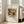 May include: Framed art print leaning against white wall next to beige sofa in bright room with large windows. Print features abstract expressionist painting with bold brushstrokes in yellows, reds, blues, and earth tones, showing dynamic flowing forms and gestural marks. Text below artwork reads "Improvisation 27" and "(1912)" on aged cream background. Light wood frame, approximately 2-3 feet tall, casting soft shadows on hardwood floor.