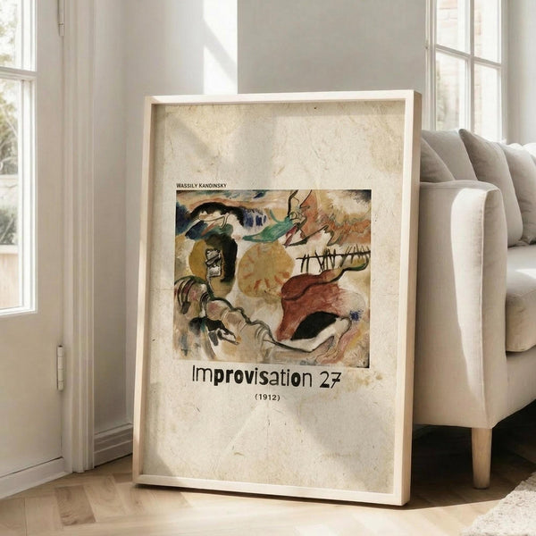 May include: Framed art print leaning against white wall next to beige sofa in bright room with large windows. Print features abstract expressionist painting with bold brushstrokes in yellows, reds, blues, and earth tones, showing dynamic flowing forms and gestural marks. Text below artwork reads "Improvisation 27" and "(1912)" on aged cream background. Light wood frame, approximately 2-3 feet tall, casting soft shadows on hardwood floor.