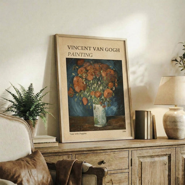 May include: Framed Van Gogh poster print featuring orange poppies in white vase against blue background, displayed on rustic wood sideboard beside fern plant, books, ceramic vase and beige upholstered chair in neutral-toned living room setting