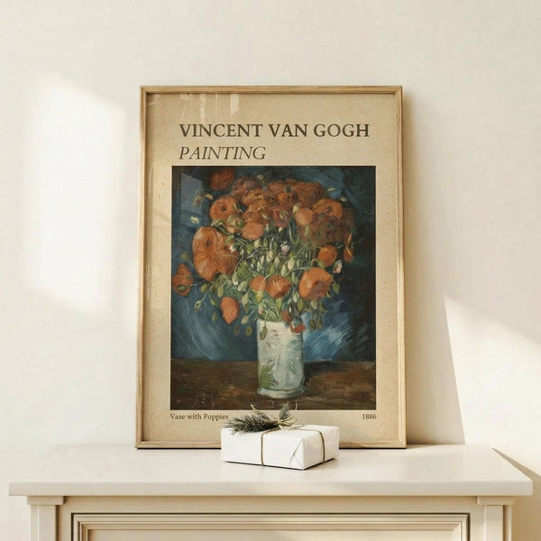 May include: Framed Van Gogh poster print featuring orange poppies in a white vase against blue background, displayed on light wood surface with small wrapped gift box decorated with greenery sprig beside it