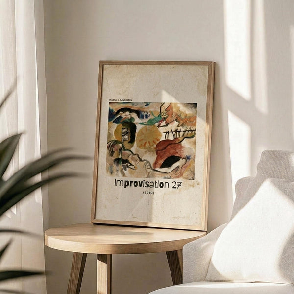 May include: Framed art print of abstract expressionist painting with colorful organic shapes in blues, greens, yellows, and reds against cream background. Print displays on round wooden side table next to beige upholstered chair. Natural sunlight creates soft shadows across white wall. Green plant leaves visible in corner. Warm, minimalist interior styling.