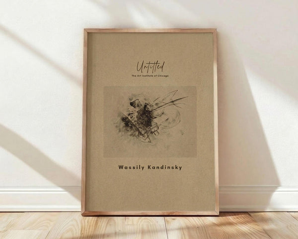 May include: Framed art print featuring an abstract Kandinsky drawing with dark ink marks and flowing lines on beige paper background, displayed in light wood frame leaning against white wall on natural wood flooring with soft window light creating diagonal shadows across the scene.