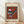 May include: Framed abstract art print in light wood frame leaning against white wall on wooden floor. Artwork features geometric shapes in rust red, teal blue, black and white - triangular forms, circles, and angular lines in modernist style. Cream matting surrounds the colorful composition. Natural lighting creates soft shadows on textured white wall.
