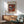 May include: Framed Kandinsky abstract art poster with geometric shapes in rust orange, featuring triangular and linear forms in black, white, and blue tones. Displayed above mid-century modern wooden credenza with white ceramic lamp, next to sage green upholstered armchair with wooden frame in sunlit room with white walls.