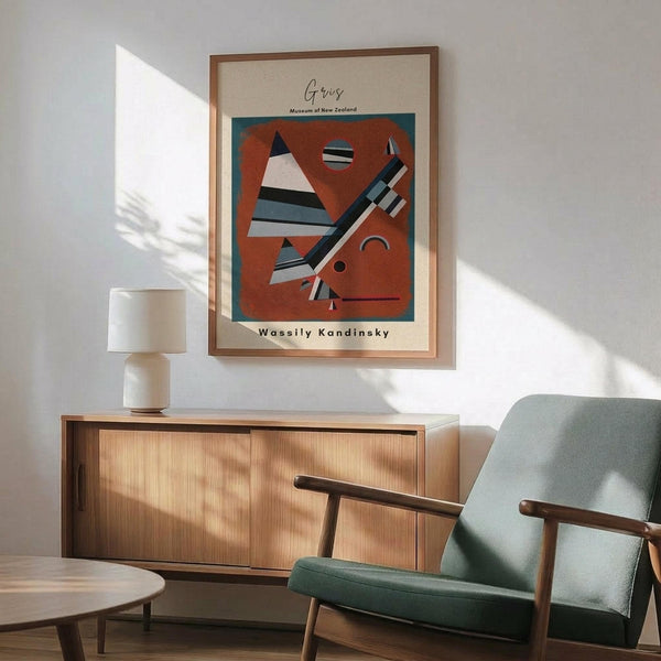 May include: Framed Kandinsky abstract art poster with geometric shapes in rust orange, featuring triangular and linear forms in black, white, and blue tones. Displayed above mid-century modern wooden credenza with white ceramic lamp, next to sage green upholstered armchair with wooden frame in sunlit room with white walls.