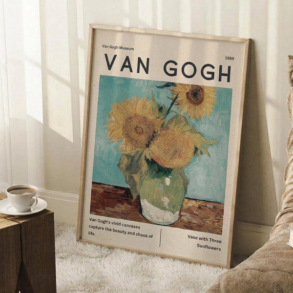 May include: Framed Van Gogh museum poster featuring three bright yellow sunflowers in a green ceramic vase against turquoise background, displayed in cozy room corner with white walls, wooden side table holding white coffee cup and saucer, cream knit throw blanket, and textured white rug