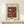 May include: Framed abstract art print in wooden frame leaning against white wall on light wood surface. The artwork features geometric shapes including striped triangles, circles, and angular forms in rust orange, teal, black, white, and gray colors. Museum exhibition poster format with "Wassily Kandinsky" text below the artwork. Small wrapped gift box with twine sits in front of the frame.