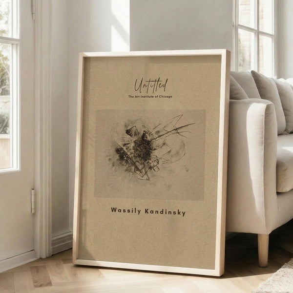 May include: Framed abstract art print with beige background featuring dark sketchy lines and organic shapes in black and brown tones. The artwork shows flowing, dynamic marks reminiscent of Kandinsky's style. White wooden frame leans against bright white wall next to beige upholstered sofa in sunlit room with large windows and hardwood floors.
