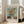 May include: Framed museum-style poster featuring Van Gogh's sunflower painting with yellow blooms in green vase against turquoise background. Light wood frame leans against white wall next to beige upholstered chair in bright, naturally-lit room with large windows and hardwood floors.