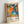 Framed exhibition poster featuring vibrant abstract artwork with colorful polka dots, floral patterns, and organic shapes in orange, blue, green, pink, and black. The poster displays dates "28. APRIL - 14. MAI 1984" at top, artist name "YAYOI KUSAMA" at bottom left, Japanese characters, and "MUSÉE D'ART MODERNE DE LA VILLE DE PARIS" below. Light wooden frame sits against white wall, casting soft shadow.