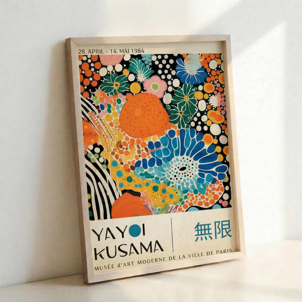 Framed exhibition poster featuring vibrant abstract artwork with colorful polka dots, floral patterns, and organic shapes in orange, blue, green, pink, and black. The poster displays dates "28. APRIL - 14. MAI 1984" at top, artist name "YAYOI KUSAMA" at bottom left, Japanese characters, and "MUSÉE D'ART MODERNE DE LA VILLE DE PARIS" below. Light wooden frame sits against white wall, casting soft shadow.