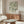 May include: Framed botanical art print with flowing green and cream leaf pattern displayed above walnut credenza in minimalist living room. Modern white sculptural chair and glass coffee table visible. Warm natural lighting creates soft shadows on neutral walls.