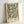 May include: Framed botanical art print with ornate green and cream floral pattern featuring flowing acanthus leaves and decorative blooms in William Morris style, displayed in light wood frame leaning against white wall with soft natural lighting creating gentle shadows
