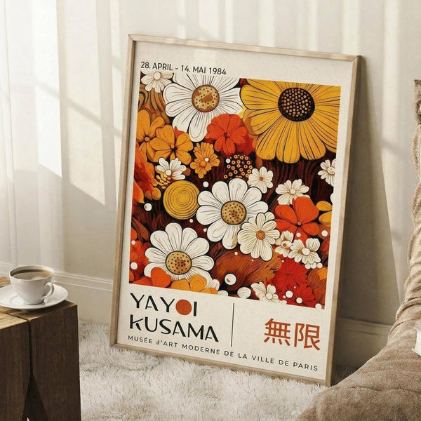 May include: Framed vintage museum exhibition poster leaning against white wall on fluffy white rug. Features colorful floral design with white daisies, orange sunflowers, and red blooms in retro 1970s style. Text shows dates April 28 - May 14, 1984 and Musée d'Art Moderne de la Ville de Paris. Natural wood frame, cozy room setting with coffee cup on wooden surface and beige blanket visible.