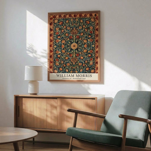 May include: Framed William Morris exhibition art print hanging on white wall above wooden sideboard with table lamp, shown next to sage green mid-century armchair and round wooden coffee table. The poster features an ornate carpet design with intricate floral patterns in deep teal, orange, and burgundy colors with decorative border, displayed in natural lighting.