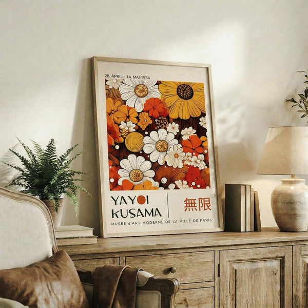 May include: Framed vintage-style art poster featuring vibrant orange, yellow, and white daisy flowers in retro 1970s design, displayed on rustic wood sideboard with books, ceramic vase, and fern plant in cozy living room setting with beige chair and neutral walls
