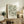 May include: Framed botanical art print with flowing green leaves in William Morris style, displayed on rustic wooden sideboard alongside fern plant, ceramic vase, and books in warm neutral living room setting with white walls and cozy seating