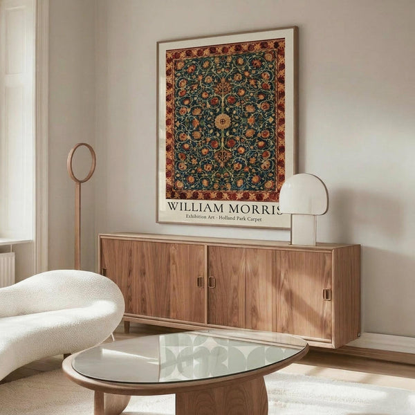 May include: Framed William Morris exhibition poster featuring intricate floral carpet design in deep teal, orange, and burgundy colors hanging above a mid-century walnut credenza. Modern living room setting with cream curved chair, glass oval coffee table, and minimalist table lamp creating warm, sophisticated interior styling.