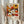 May include: Hands holding a framed vintage exhibition poster featuring colorful retro flowers in orange, yellow, white and red tones against a dark background. The artwork shows daisies, sunflowers and abstract blooms with dotted centers. Light wood frame against soft neutral curtains with dried pampas grass visible to the left. The poster displays museum exhibition text and Japanese characters at the bottom.