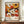 May include: Framed exhibition poster featuring colorful floral artwork with white daisies, orange and yellow sunflowers, and red blooms in retro 1970s style. Text shows dates "28. APRIL - 14. MAI 1984" and "YAYOI KUSAMA" with Japanese characters and "MUSÉE D'ART MODERNE DE LA VILLE DE PARIS". Poster displayed on wooden sideboard next to white ceramic vase and books in neutral-toned room with white walls and trim.