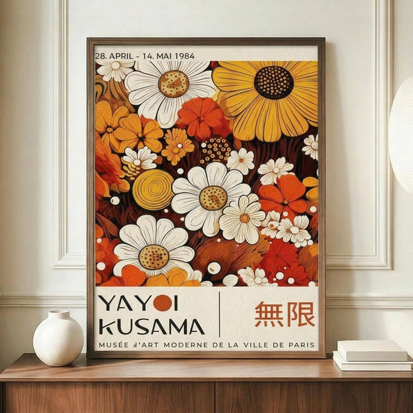 May include: Framed exhibition poster featuring colorful floral artwork with white daisies, orange and yellow sunflowers, and red blooms in retro 1970s style. Text shows dates "28. APRIL - 14. MAI 1984" and "YAYOI KUSAMA" with Japanese characters and "MUSÉE D'ART MODERNE DE LA VILLE DE PARIS". Poster displayed on wooden sideboard next to white ceramic vase and books in neutral-toned room with white walls and trim.