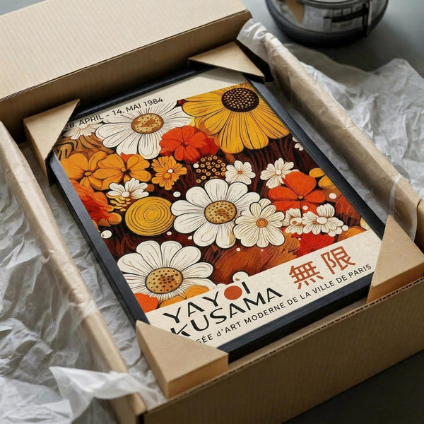 A framed poster of a colorful floral design, with the text "YAYOI KUSAMA" and "SEEE A ART MODERNE DE LA VILLE DE PARIS" printed on it. The poster is displayed in a cardboard box, which is wrapped in bubble wrap.