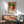 May include: Framed botanical art print featuring vibrant orange and red chrysanthemum flowers with teal and green foliage in William Morris style, displayed above a wooden sideboard with lamp in modern living room with mint green mid-century chair and natural sunlight streaming across white walls.