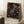 May include: Framed art print leaning against white wall corner featuring colorful dot painting on black background with vibrant circles, spirals and organic patterns in rainbow hues. Japanese text at bottom reads Yayoi Kusama with Tokyo below. Natural wood frame, displayed near white coffee cup on wooden block and beige knit throw on white textured rug.