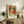 May include: Framed botanical art print featuring vibrant orange and coral flowers with teal and green foliage in decorative swirling patterns, displayed on rustic wooden sideboard alongside fern plant, ceramic vase, and books in neutral-toned living room setting with beige upholstered furniture and soft natural lighting.