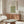 May include: William Morris botanical poster with blue and green vine pattern displayed above wooden sideboard in minimalist living room. Framed print shows intricate floral design with turquoise and olive colors. Scene includes cream upholstered chair, glass-top coffee table, and modern brass lamp on credenza.