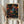 May include: Hands holding a framed art print featuring Yayoi Kusama's colorful dot painting on black background with swirling patterns in vibrant blues, oranges, pinks, and yellows. Print shows "YAYOI KUSAMA" and "TOKYO" text below artwork. Person wearing cream ruffled sleeves holds wooden-framed poster against white curtained window with dried pampas grass visible to the side.