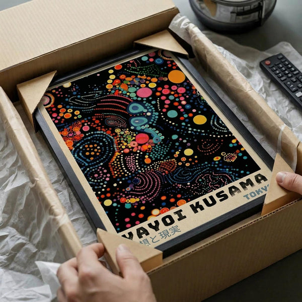 A person's hands are holding a cardboard box containing a framed poster with a colorful abstract design.