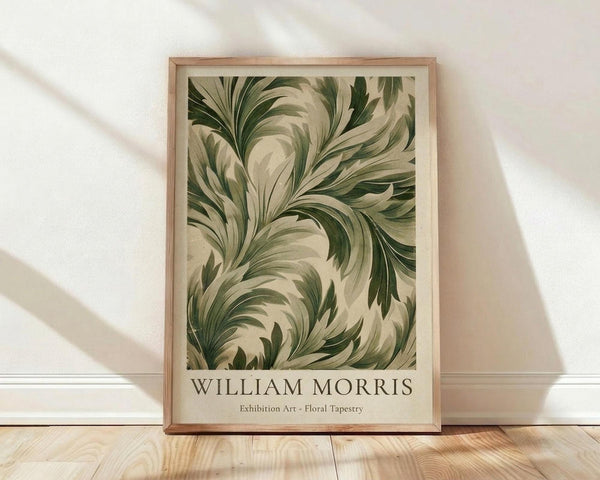 May include: Framed botanical poster featuring flowing green and cream colored leaves in an ornate, swirling pattern reminiscent of Art Nouveau design. The artwork is displayed in a light wood frame against a white textured wall with natural lighting creating soft shadows. The print sits on light wooden flooring, showing the full vertical rectangular format with text at the bottom identifying it as exhibition art.
