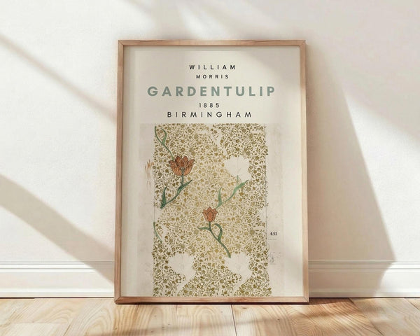 May include: Framed botanical poster with William Morris Garden Tulip design from 1885 Birmingham, featuring delicate orange tulips on intricate olive green damask pattern background, displayed in light wood frame against white wall on wooden floor with natural window lighting creating soft shadows