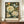 May include: Framed botanical art print displayed on wooden sideboard featuring large cream peonies, blue butterfly, and smaller flowers on dark background with William Morris exhibition text below. White ceramic vase and books sit nearby against beige paneled wall.