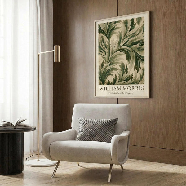 May include: Framed botanical print with flowing green foliage pattern in cream and sage colors, displayed on wood-paneled wall above beige upholstered armchair with geometric throw pillow. Modern brass floor lamp and dark side table with open book nearby. Neutral-toned contemporary living room setting with natural lighting from window.