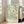 May include: Large framed botanical art print featuring flowing green leaf patterns on cream background, displayed on hardwood floor against white wall next to beige upholstered sofa with natural lighting from tall windows creating soft shadows across the bright, minimalist living room interior.