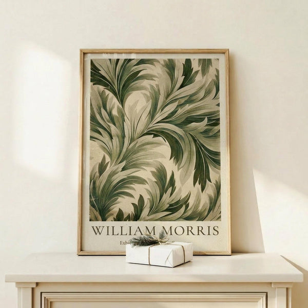 May include: Framed botanical art print featuring flowing green and cream acanthus leaf pattern in William Morris style, displayed on light wood console table with small white wrapped gift beside it, against neutral wall in minimalist room setting