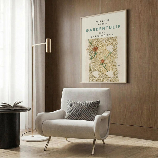May include: Framed botanical poster with cream background featuring orange tulips and decorative golden scrollwork pattern, displayed on wood-paneled wall above beige upholstered armchair with geometric patterned pillow, brass floor lamp, and round black side table with open book in modern neutral-toned interior setting.